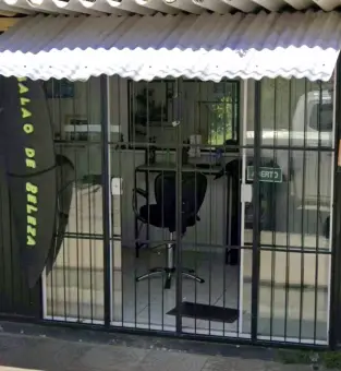 Porta de entrada do salão com a cadeira de corte vista pela grade